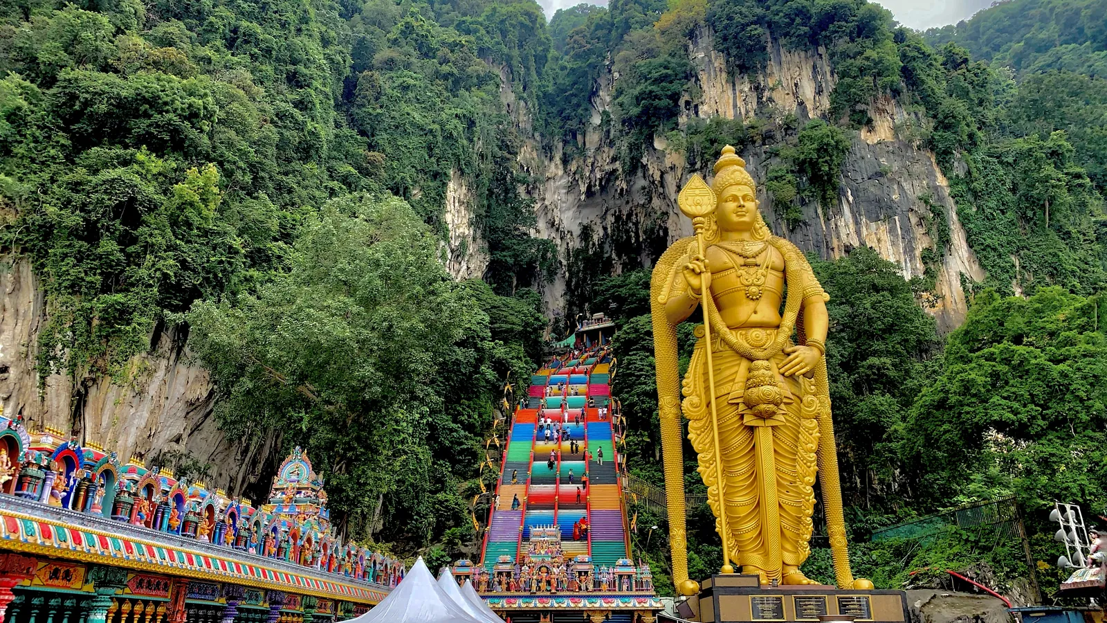 Golden Lord Murugan statue beside the rainbow-painted staircase and limestone cliffs at Batu Caves, Selangor