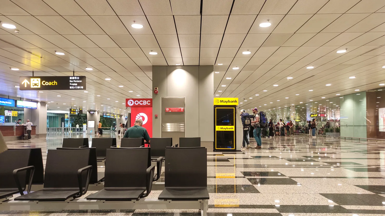 Arrival hall at Singapore Changi Airport with rows of seats, bank kiosks and a sign pointing to the coach pick-up
