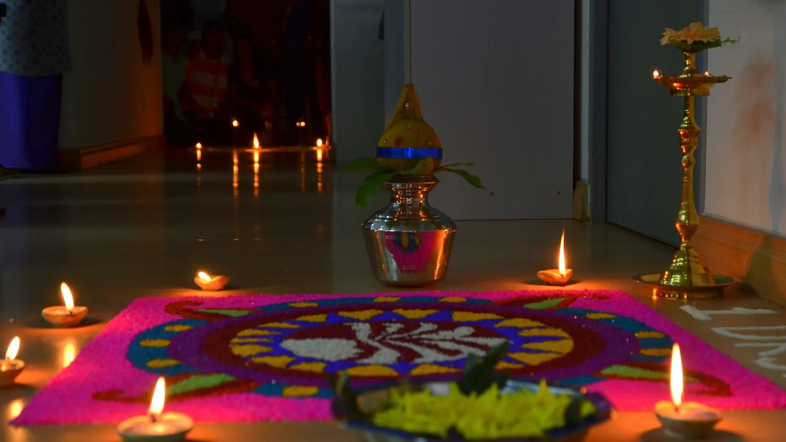 Deepavali kolam of coloured rice with lit clay oil lamps and a brass lamp in a Malaysian home