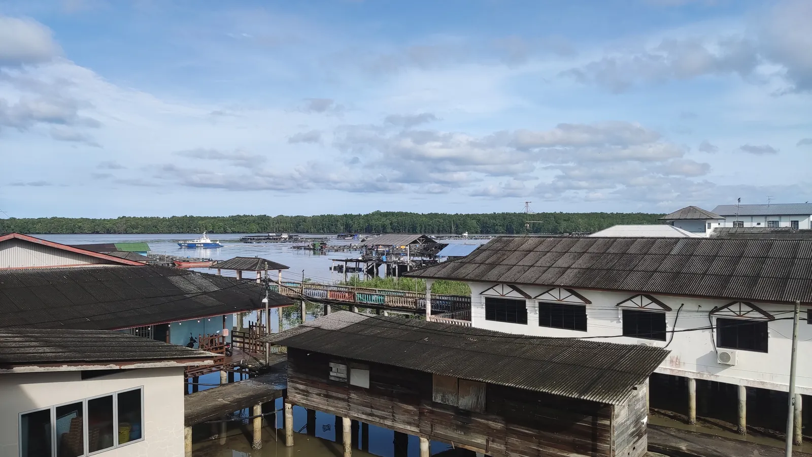 Wooden and concrete houses on stilts over the water at Kukup Laut fishing village, Johor, with fish farms and the mangroves of Pulau Kukup behind