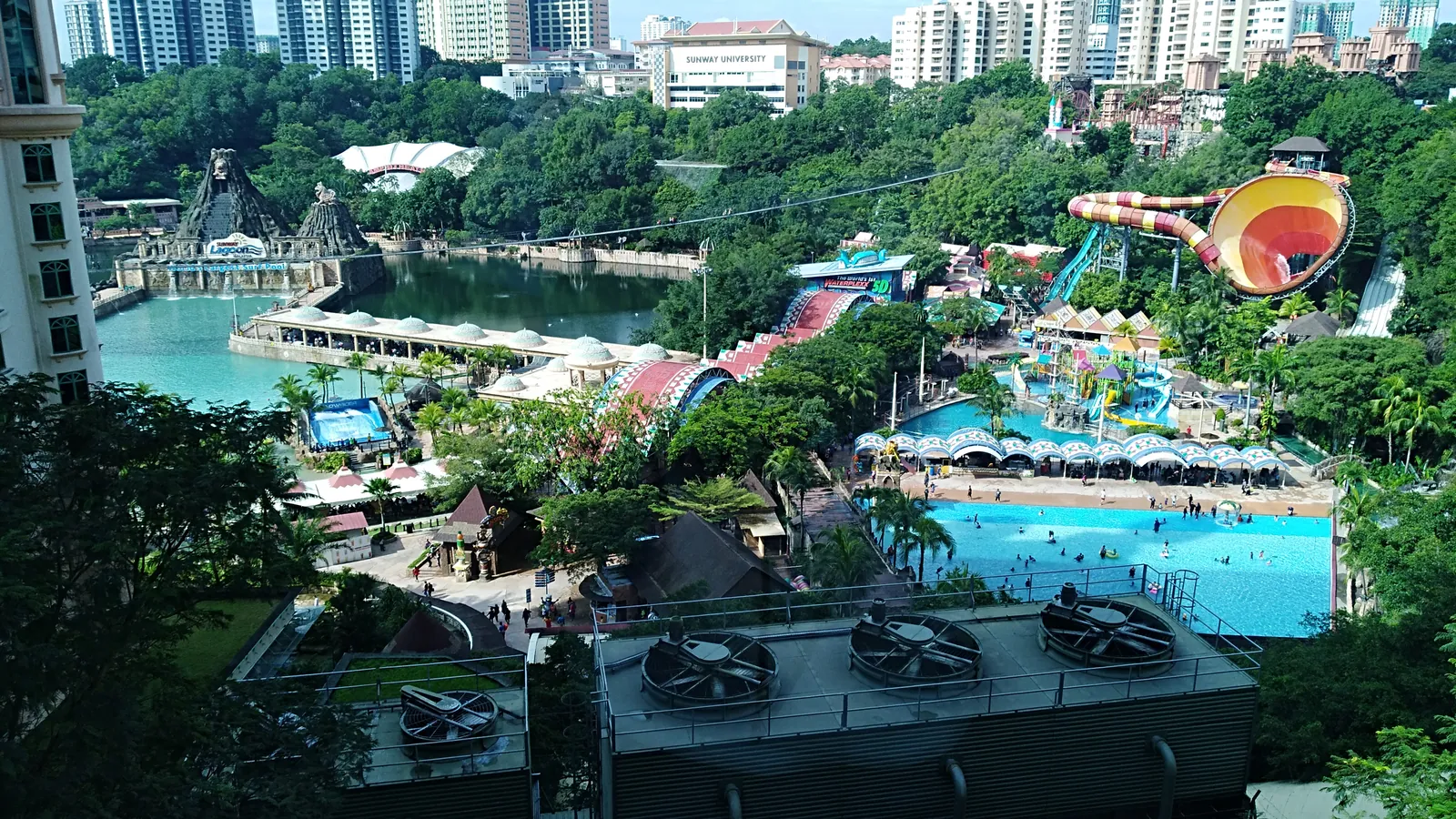 Wave pool, colourful water slides and a man-made lake at Sunway Lagoon theme park, surrounded by trees and high-rise buildings in Bandar Sunway
