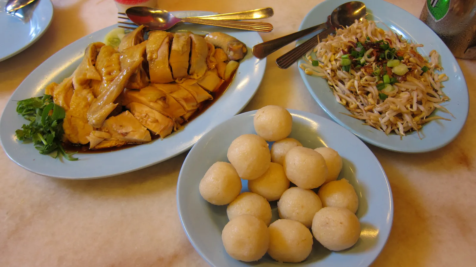 A plate of Melaka chicken rice balls with steamed chicken and bean sprouts on a marble table