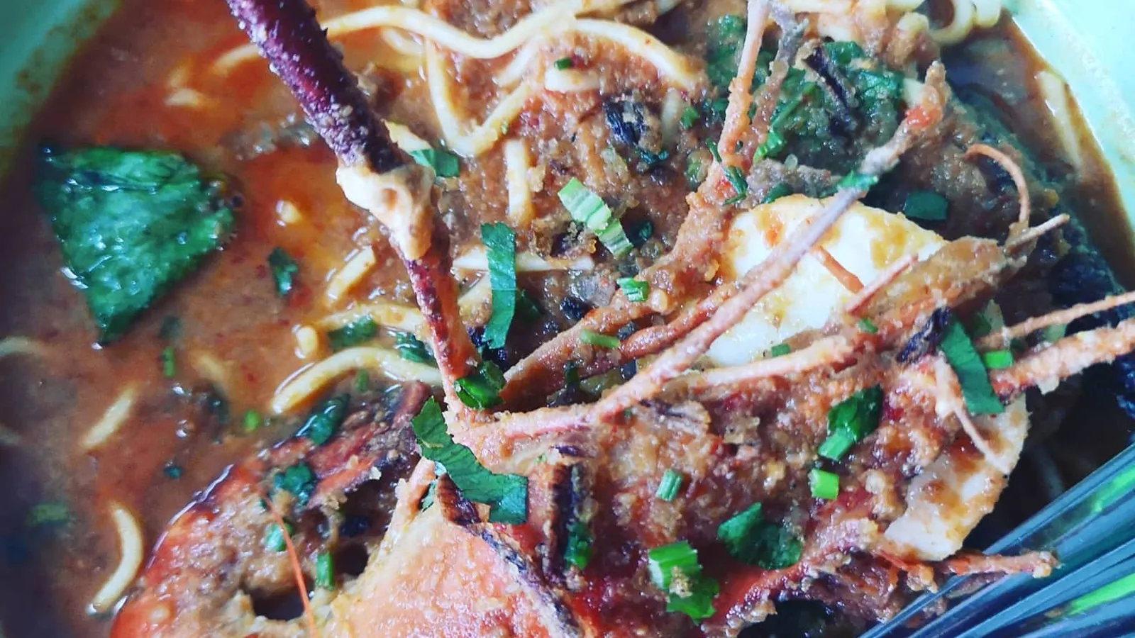 Close-up of a bowl of mee bandung in Muar, Johor, with yellow noodles, a large grilled prawn, egg and spring onions in thick red gravy