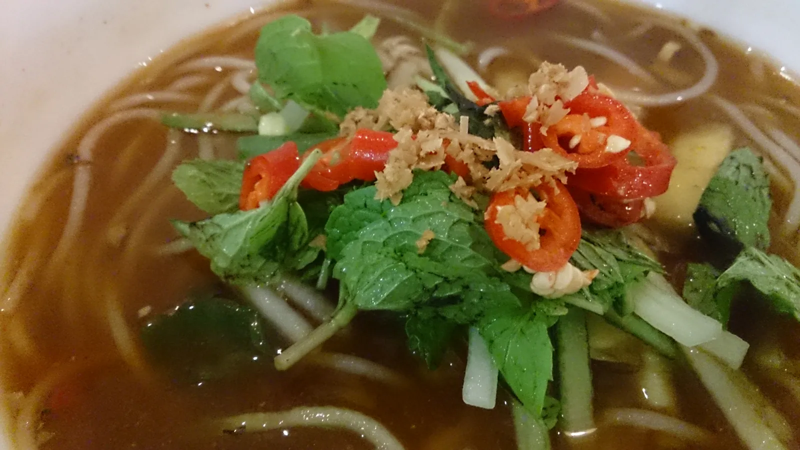 Bowl of Penang-style assam laksa topped with fresh mint, sliced red chilli, cucumber and shallots in a sour fish broth