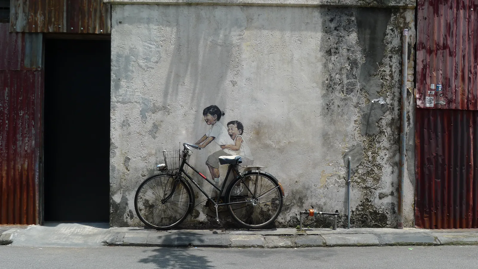 Little Children on a Bicycle mural by Ernest Zacharevic, with a real bicycle fixed to a weathered wall on Armenian Street, George Town, Penang