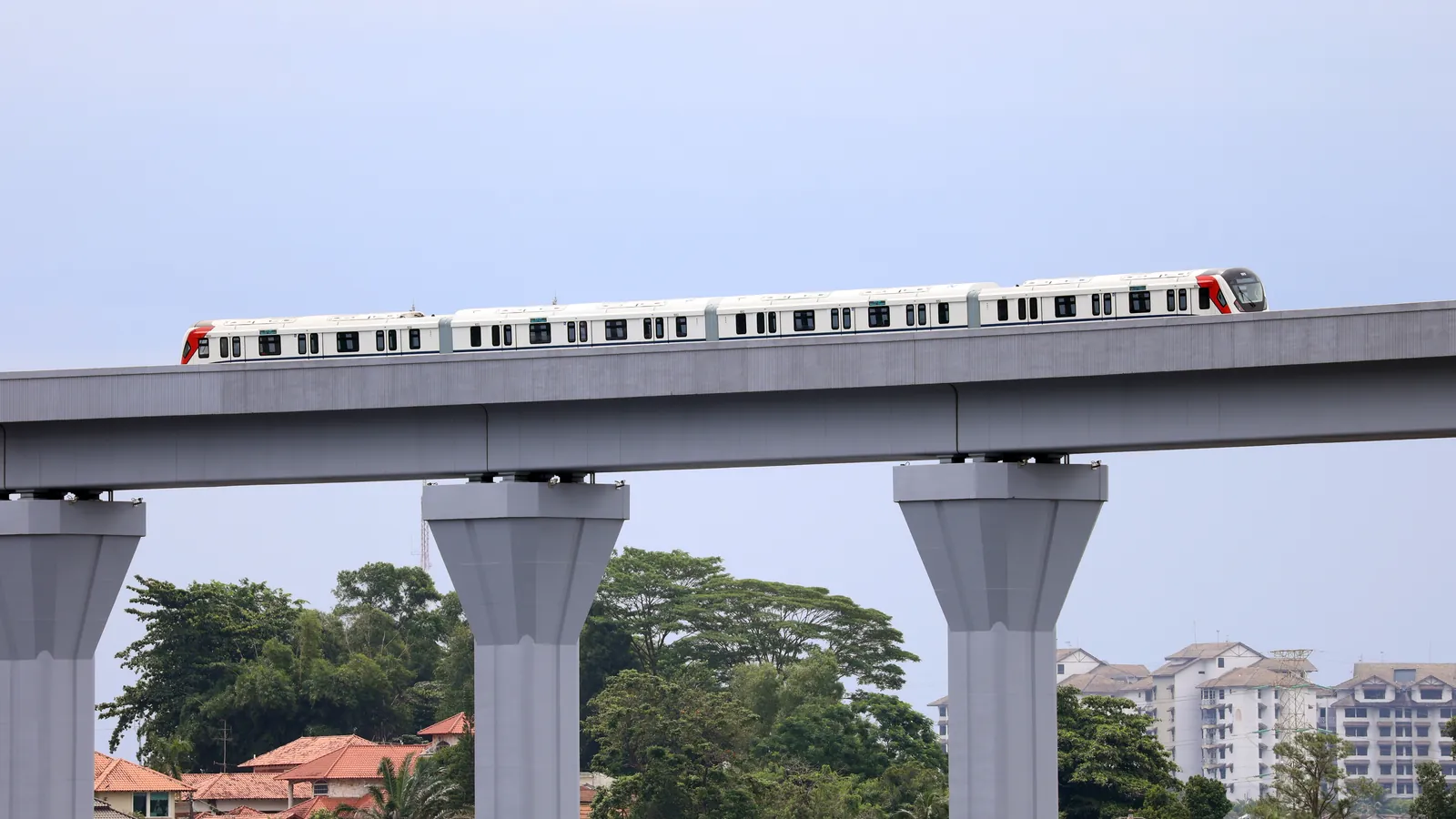 RTS Link train running on its elevated viaduct during trial runs, with houses and trees of Johor Bahru below