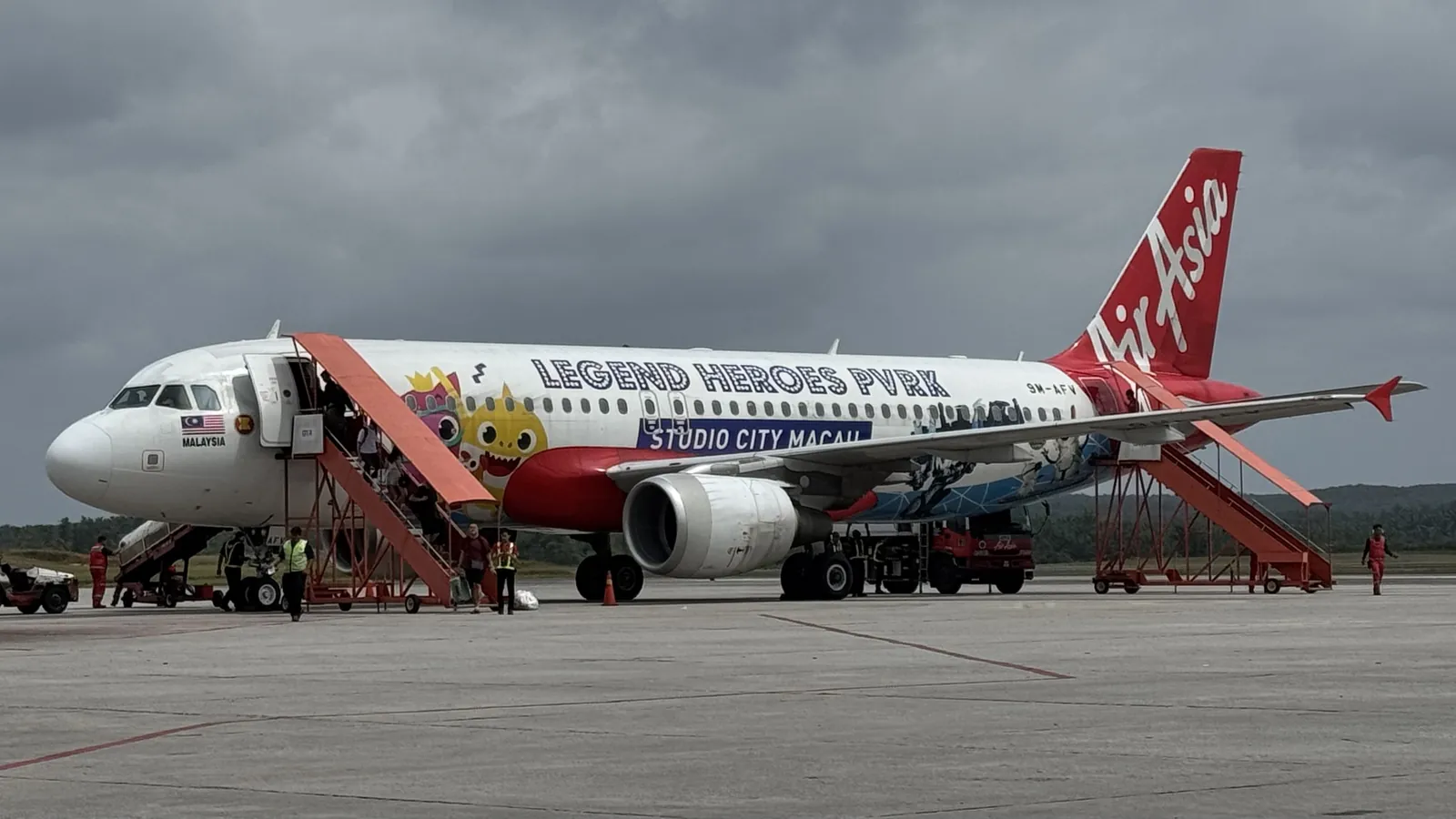 AirAsia Airbus A320 parked on the apron at Senai International Airport with boarding stairs attached