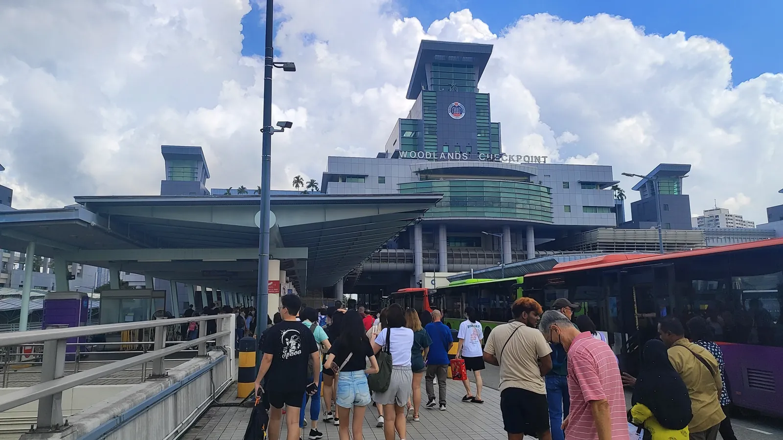 Travellers walking towards the Woodlands Checkpoint building in Singapore on a sunny day