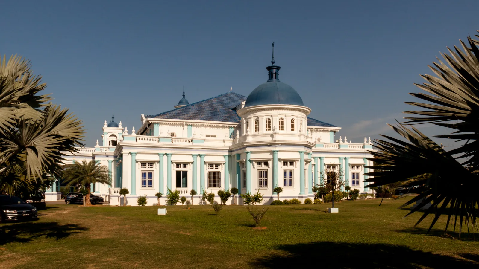 Sultan Ibrahim Jamek Mosque in Muar, Johor, a white and pale-blue colonial-style building with a blue dome, seen across a lawn with palm trees