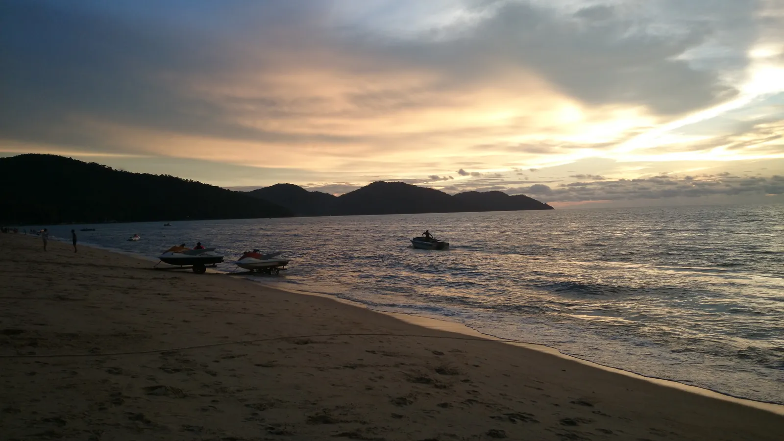 Sunset over Batu Ferringhi beach on Penang’s north coast, with jet skis on the sand and green hills across the bay