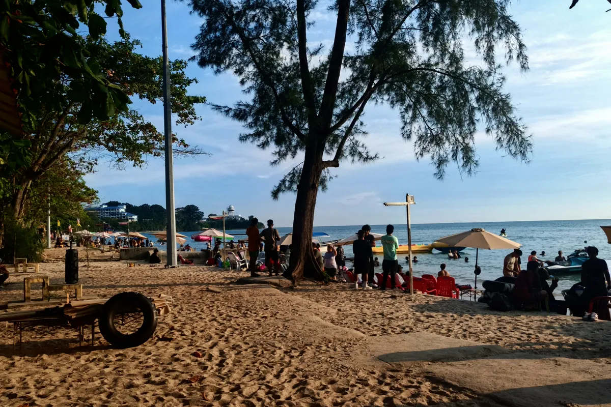 Visitors relaxing on the sand under trees at Teluk Kemang Beach, Port Dickson